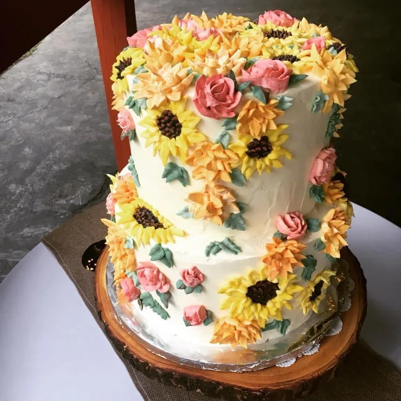 two tier wedding cake with roses and sunflowers in buttercream frosting